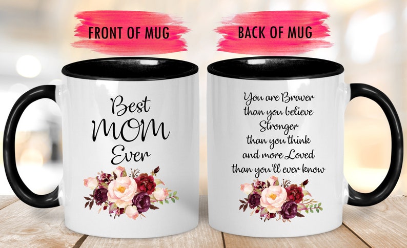 May include: White ceramic mug with a black handle and rim. The front of the mug reads "Best MOM Ever" with a floral design. The back of the mug has a quote about strength and love, also with a floral design.