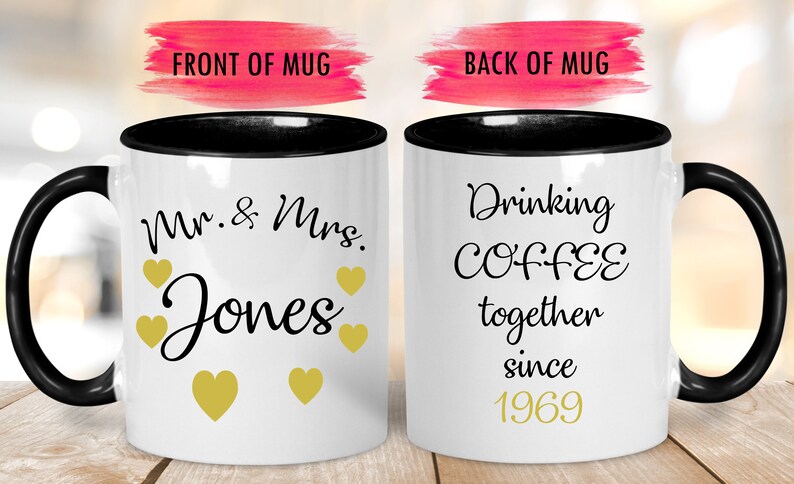 May include: Two white coffee mugs with black rims. The front mug has the text "Mr. & Mrs. Jones" with gold hearts. The back mug has the text "Drinking COFFEE together since 1969" with gold text.