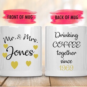 May include: Two white coffee mugs with black text. The front mug says "Mr. & Mrs. Jones" with gold hearts. The back mug says "Drinking COFFEE together since 1969".