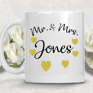 May include: White ceramic mug with a black inscription that reads "Mr. & Mrs. Jones" and gold hearts around the text.
