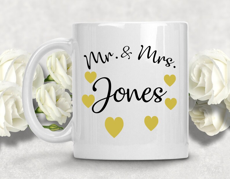May include: White ceramic mug with a black inscription that reads "Mr. & Mrs. Jones" and gold hearts around the text.