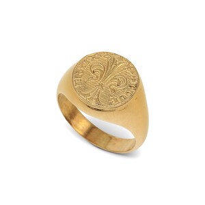 May include: A gold signet ring with a round face featuring a fleur-de-lis design and the inscription "ERIT IN COELLO"