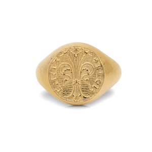 May include: A gold signet ring with a detailed design of a fleur-de-lis and the inscription "Fidelitas" around the edge.