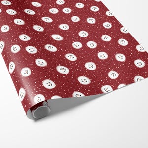 Puede incluir: Papel de regalo rojo con un patr&oacute;n repetido de mu&ntilde;ecos de nieve blancos con ojos y bocas negros. El fondo es rojo oscuro con puntos blancos.