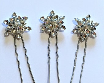 Könnte beinhalten: Drei silberne Haarnadeln mit Kristallblumen-Akzenten. Jede Nadel hat ein blumenförmiges Design mit klaren Strasssteinen.