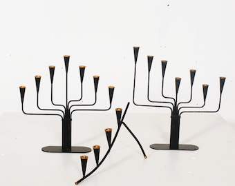 May include: Black metal candelabras with gold-colored accents. The candelabras have multiple arms, each holding a candle cup. The design is minimalist and modern, with a sleek, elegant appearance. The candelabras are suitable for holding multiple candles.