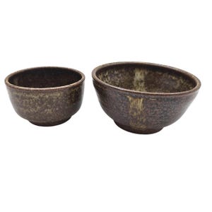 Puede incluir: Dos cuencos de cerámica con un esmalte marrón moteado. Los cuencos tienen un aspecto rústico, con variaciones de color y textura. Los cuencos son de diferentes tamaños, siendo uno más pequeño y redondeado que el otro.