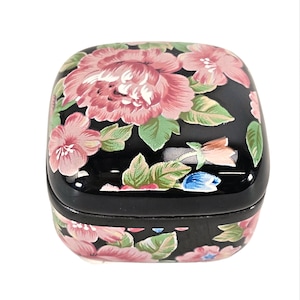 Pode incluir: Uma caixa de joias quadrada preta com um design floral. A caixa é decorada com flores rosa e verdes sobre um fundo preto.