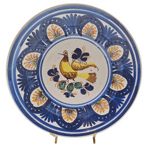 Puede incluir: Un plato de cerámica blanca con un diseño floral azul y amarillo. El centro del plato presenta un pájaro amarillo con detalles azules y verdes.