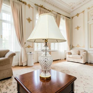 May include: A table lamp featuring a clear, cut-glass base with a diamond-patterned texture and a gold-toned metal circular base. The lamp is topped with a cream-colored, conical fabric lampshade that has a braided trim along the edges.