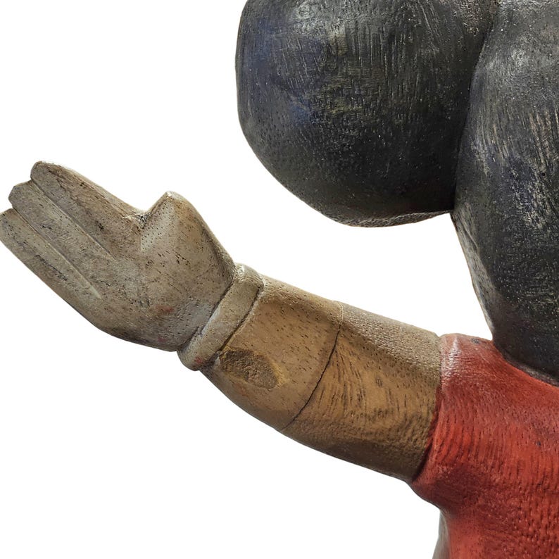 K&ouml;nnte beinhalten: Eine geschnitzte Holzfigur mit erhobener Hand. Der Arm ist braun mit einem roten Hemd und einem schwarzen Kopf. Die Hand ist hellbraun mit sichtbarer Holzmaserung.