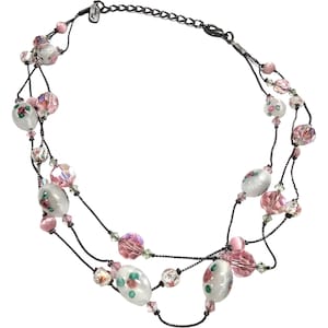 May include: A multi-strand necklace with pink and white glass beads. The beads are decorated with floral patterns. The necklace is made of black cord.