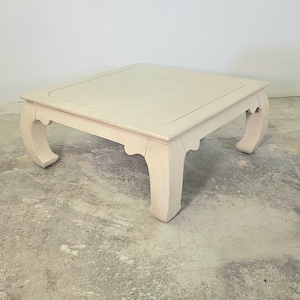 May include: A square, off-white coffee table with curved legs. The table has a textured surface and a decorative edge. The legs are a unique, curved design. The table is approximately 30 inches wide and 16 inches tall.