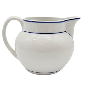 Puede incluir: Jarra de cerámica blanca con cuerpo redondeado, asa curva y pico vertedor. La jarra está adornada con una fina línea azul alrededor del borde y la base. Un diseño clásico y elegante para servir bebidas.