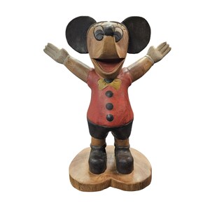 K&ouml;nnte beinhalten: Eine Holzfigur einer Zeichentrickmaus mit ausgestreckten Armen. Die Maus hat gro&szlig;e schwarze Ohren, ein rotes Hemd mit schwarzen Kn&ouml;pfen, schwarze Shorts und schwarze Schuhe. Eine gelbe Fliege und ein Holzsockel vervollst&auml;ndigen das Design.