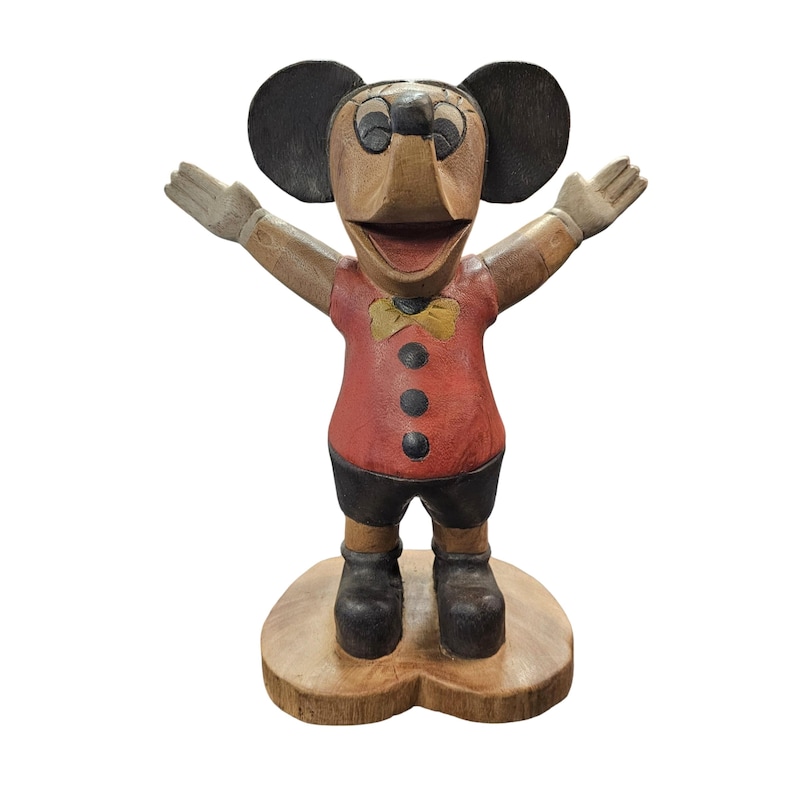 K&ouml;nnte beinhalten: Eine Holzfigur einer Zeichentrickmaus mit ausgestreckten Armen. Die Maus hat gro&szlig;e schwarze Ohren, ein rotes Hemd mit schwarzen Kn&ouml;pfen, schwarze Shorts und schwarze Schuhe. Eine gelbe Fliege und ein Holzsockel vervollst&auml;ndigen das Design.