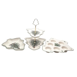 May include: A set of Christmas-themed serving dishes. The set includes a two-tiered server, a rectangular dish, and a muffin tin, all shaped like Christmas trees. Each piece is white with a green trim and a Christmas tree design.