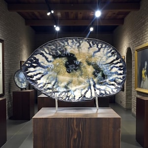 May include: A white ceramic mug with a black handle and the text "But First, Coffee" in a black, handwritten-style font. The mug is on a white surface.