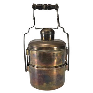 May include: A vintage brass tiffin carrier with a wooden handle and two stacked containers. The carrier has a worn, antique finish.