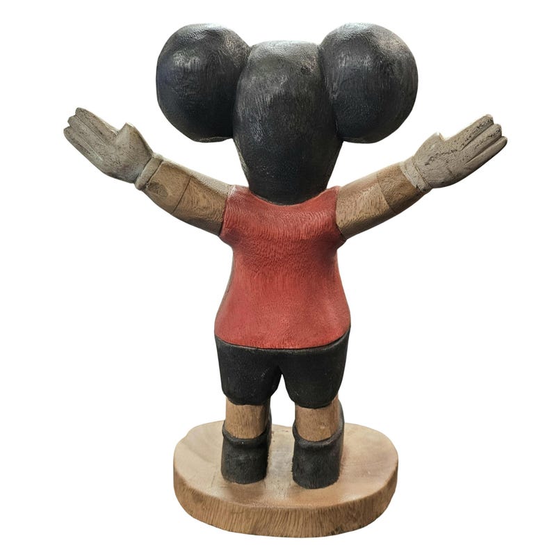 K&ouml;nnte beinhalten: Holzskulptur einer Figur mit gro&szlig;en, runden Ohren und ausgestreckten Armen. Die Figur tr&auml;gt ein rotes Hemd, schwarze Shorts und steht auf einem Holzsockel. Die Arme und H&auml;nde sind hellere Holzfarben.