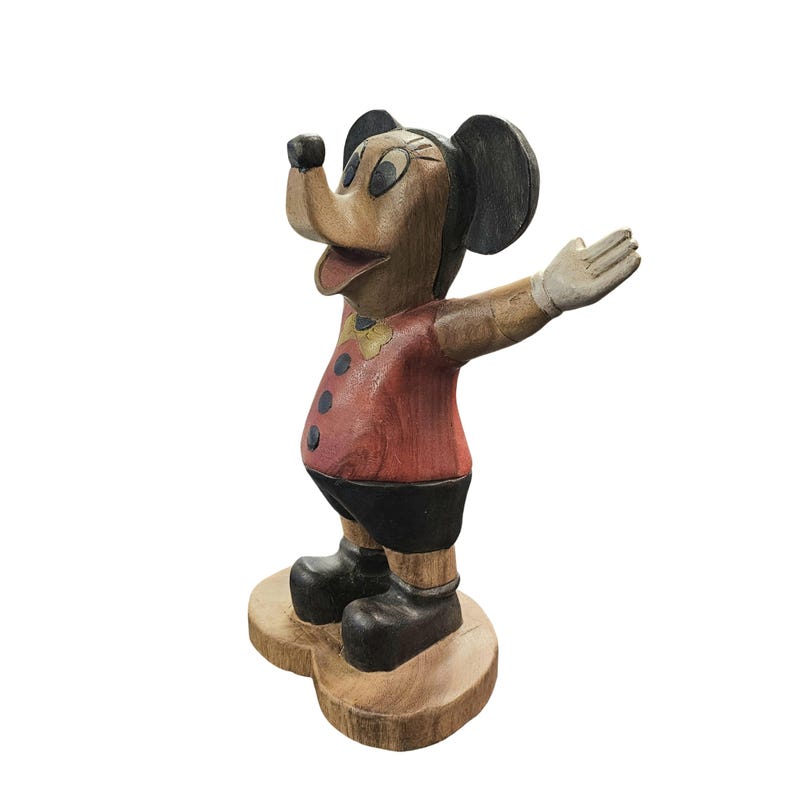 K&ouml;nnte beinhalten: Holzfigur von Mickey Mouse mit ausgestreckten Armen. Die Figur ist in Rot, Schwarz und Beige bemalt, mit einem roten Hemd, schwarzen Shorts und schwarzen Schuhen. Der Sockel hat eine nat&uuml;rliche Holzfarbe.