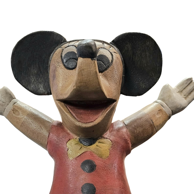 K&ouml;nnte beinhalten: Eine Holzfigur einer Mausfigur mit gro&szlig;en schwarzen Ohren, einem roten Hemd und einer gelben Fliege. Die Maus hat die Arme ausgestreckt und einen l&auml;chelnden Ausdruck. Die Figur ist aus Holz geschnitzt und hat ein Vintage-Aussehen.