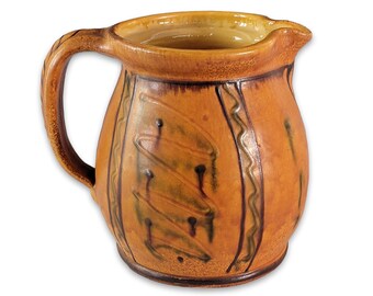 May include: A brown ceramic pitcher with a green and brown geometric design. The pitcher has a rounded body and a handle.