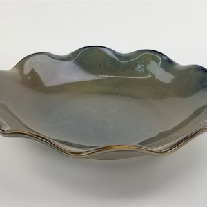 May include: A ceramic serving bowl with a wavy, scalloped rim. The bowl has a gradient of colors, transitioning from a dark green to a light blue-gray. The rim is trimmed with a metallic gold finish, adding a touch of elegance to the piece.