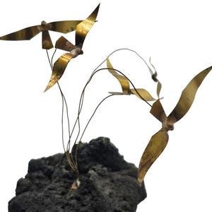 May include: A sculpture of several brass birds in flight, attached to thin wires and mounted on a dark, textured base. The birds have outstretched wings, and the sculpture has a natural, artistic aesthetic.