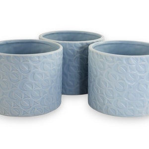 Puede incluir: Tres macetas de cerámica azul claro con un patrón en relieve. Las macetas son redondas y tienen un acabado liso y esmaltado.
