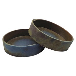 May include: Two handmade ceramic bowls with a rustic, earthy aesthetic. The bowls are round with a low profile and a wide rim. One bowl is dark blue, and the other is a mottled brown and green. The bowls are slightly overlapping.