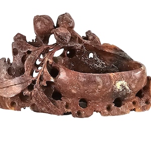 Puede incluir: Una escultura de piedra tallada de una rama frondosa con un cuenco en el centro. La escultura está hecha de piedra marrón rojiza con una textura natural y rugosa.