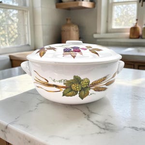 May include: White ceramic serving bowl with lid. The bowl features a decorative design of wheat, hops, and berries in shades of green, brown, and purple. The bowl has two handles and a knob on the lid.
