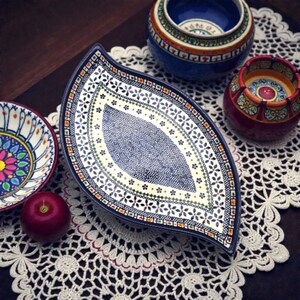 May include: A collection of decorative ceramic bowls and plates with intricate floral patterns. The centerpiece is a leaf-shaped platter with a blue and white design. Other bowls are blue, red, and white, with a red apple on the side.