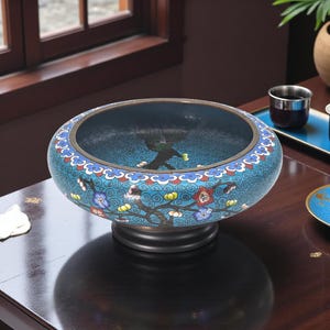 Puede incluir: Un cuenco decorativo ovalado con un diseño floral azul. El cuenco tiene una base marrón oscuro y un patrón detallado de flores y remolinos en tonos de azul, rojo y blanco. El interior del cuenco es de un azul más oscuro.