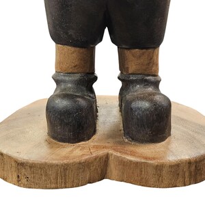 K&ouml;nnte beinhalten: Holzgeschnitzte Figur mit dunklen Stiefeln und Hosen, helleren Beinen und einem Holzsockel. Die Figur hat ein rustikales, handwerkliches Aussehen. Die Stiefel haben eine strukturierte Oberfl&auml;che.
