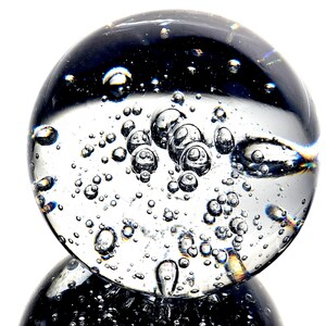 May include: A clear glass sphere with many small air bubbles trapped inside. The sphere is sitting on a black surface.