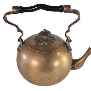 Puede incluir: Una tetera de latón antigua pequeña con un asa negra y un diseño floral decorativo en la tapa.