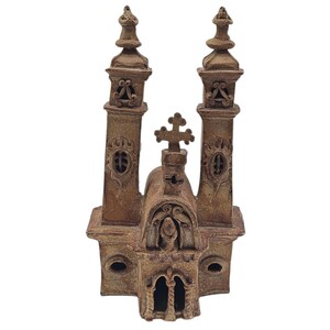 May include: A detailed, brown ceramic church model with two tall spires and a central cross. The model features arched windows, decorative carvings, and a textured surface, showcasing a vintage aesthetic.