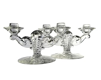 May include: A pair of clear glass candle holders with ornate designs. Each holder has three candle cups and a wide base.