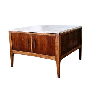 May include: A mid-century modern coffee table with a white marble top and two wooden doors. The table has a light wood frame and legs.