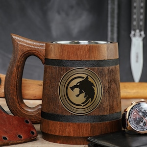 May include: A wooden beer stein with a stainless steel interior and a black wolf emblem. The stein is surrounded by a leather-wrapped axe, a watch, and a leather wallet.