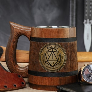 May include: A wooden beer stein with a stainless steel interior. The stein has a black band around the top and a gold metal emblem with a dice and the text "Well, Shit" on the front.