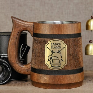 May include: A wooden beer stein with a stainless steel interior. The stein has a black band around the top and bottom and a metal plaque with the words "Ragged Flagon" and a graphic of a beer mug with crossed swords.