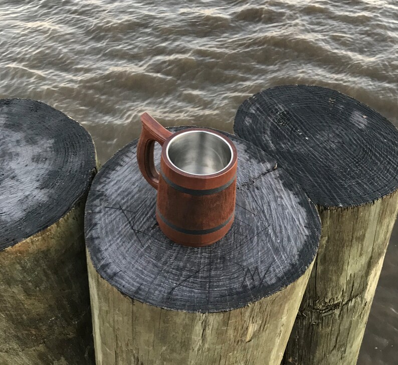 May include: A wooden beer stein with a stainless steel interior. The stein is sitting on a wooden surface.