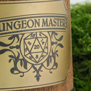 May include: A gold-colored metal plaque with the words "Dungeon Master" and a black and white illustration of a twenty-sided die.