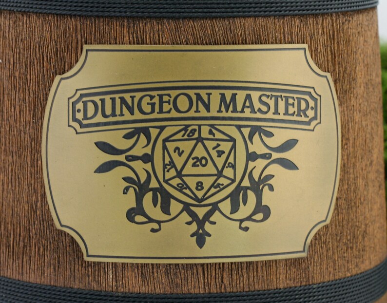 May include: A gold-colored metal plaque with a black inscription that reads "DUNGEON MASTER" and a black and white illustration of a twenty-sided die.
