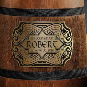 May include: A wooden beer stein with a gold-colored metal plaque. The plaque has a Celtic knot design and the text "Groomsman Robert 12 Aprile 2019".