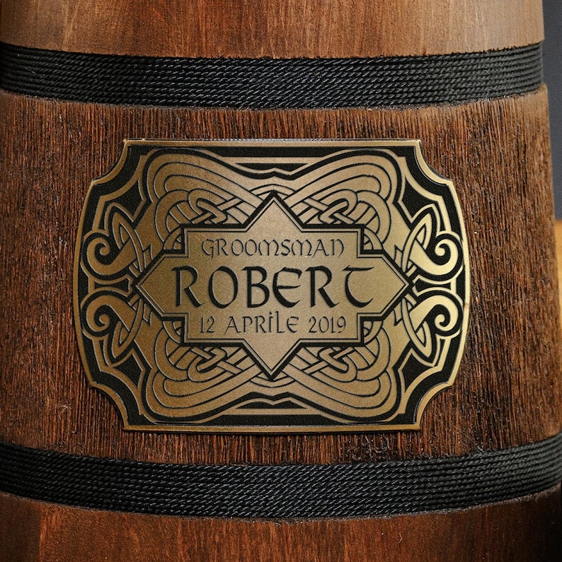 May include: A wooden beer stein with a gold-colored metal plaque. The plaque has a Celtic knot design and the text "Groomsman Robert 12 Aprile 2019".