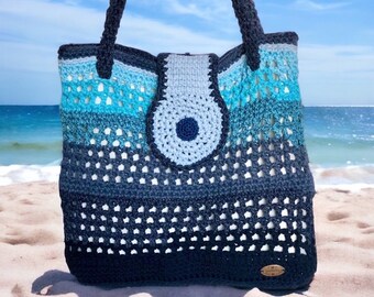 May include: A blue and gray crocheted tote bag with a large eye design on the front. The bag has a woven texture and a wide, sturdy strap.